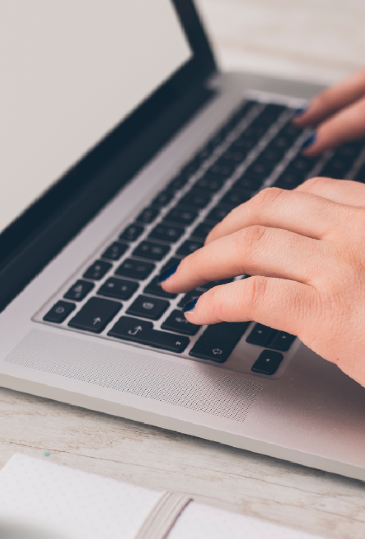 A pair of female hands with black nail polish typing on a laptop keyboard.